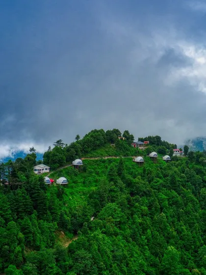 A wide-angle photograph of the Kanatal domes under a dramatic, cloudy sky. This shot emphasizes the raw, natural beauty of the location and the feeling of being immersed in the mountains.