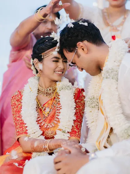 A tender moment during a South Indian wedding ceremony, where the couple shares a smile as rice is showered upon them, highlighting the beauty of cultural traditions.