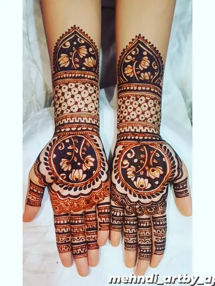 This design features a large, circular mandala on the palm filled with delicate floral vines. The pattern on the forearms uses a 'jaali' or net effect, creating a beautiful contrast in textures.