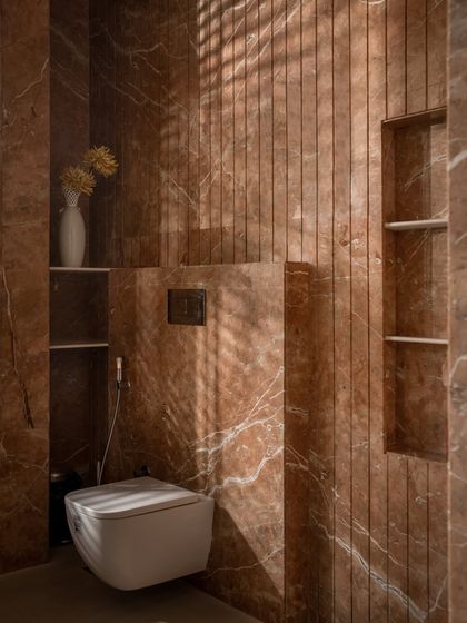 A detail of the terracotta marble in the bathroom, showing the built-in shelving and the way light interacts with the vertically grooved stone. The design is both functional and highly textural.
