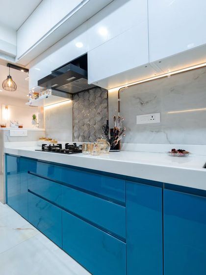 The combination of glossy blue cabinets, a white countertop, and a textured backsplash creates a visually interesting and highly modern kitchen space.