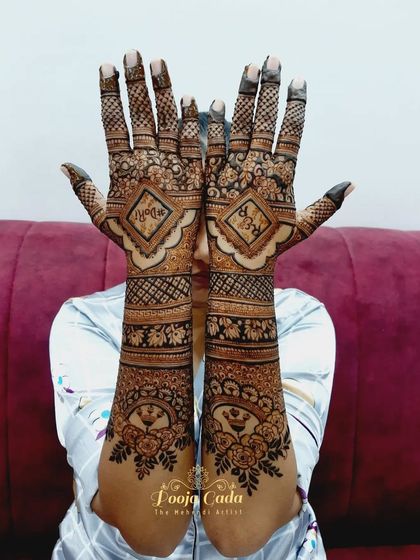A beautiful example of a back-hand engagement design. The initials of the couple are placed inside diamond-shaped frames, surrounded by floral patterns and topped with peacock motifs.