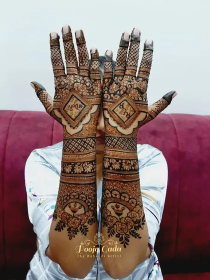 A beautiful example of a back-hand engagement design. The initials of the couple are placed inside diamond-shaped frames, surrounded by floral patterns and topped with peacock motifs.