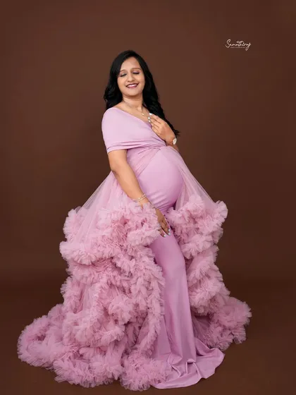 A joyful portrait of a mother-to-be in a lavender gown with a ruffled train. Her happy expression and the elegant dress create a beautiful and celebratory image.