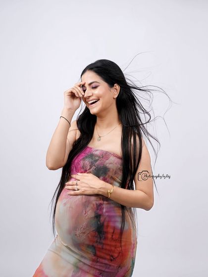 A candid and joyful studio portrait of a mother-to-be in a colorful abstract dress.