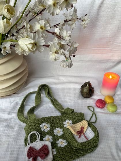 A beautifully styled shot of our green daisy book cover with a sling, shown with a matching small pouch and an AirPod case.