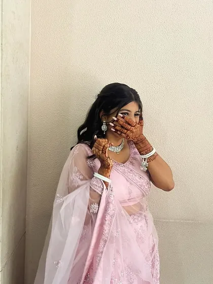 A candid moment of a happy client, her hands adorned with a deep henna stain. The color looks stunning against her beautiful pink outfit.