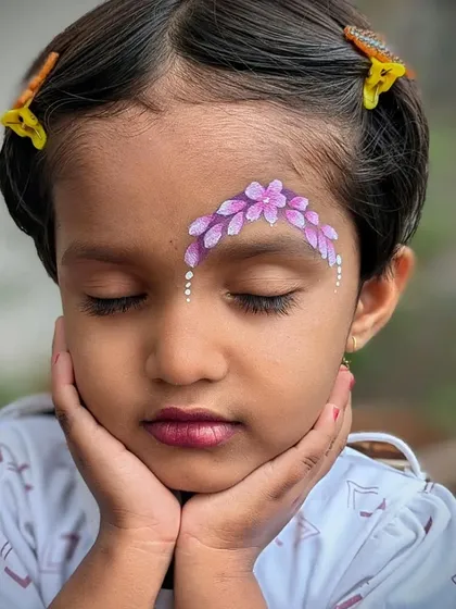 A serene moment captured, showing a delicate purple floral design painted across a child's forehead.