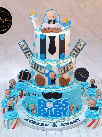 A grand three-tier Boss Baby cake for twins' first birthday. This 6kg chocolate cake is surrounded by matching themed cupcakes, creating an impressive dessert spread.