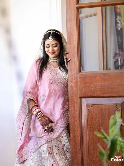 A lovely portrait of the bride in her pastel pink lehenga, peeking through a doorway.