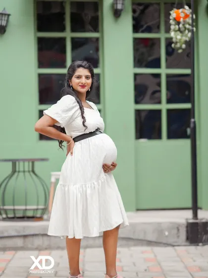 A confident solo portrait of the mother-to-be in a white dress, showcasing her baby bump.