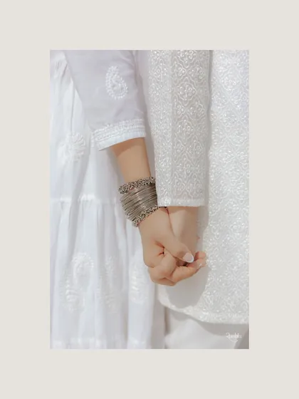 A simple, beautiful detail of the couple holding hands, their matching white chikankari outfits symbolizing their unity.