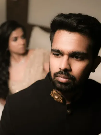 A groom's portrait with an editorial feel. The focus is on his pensive expression, with the bride blurred in the background, telling a story.