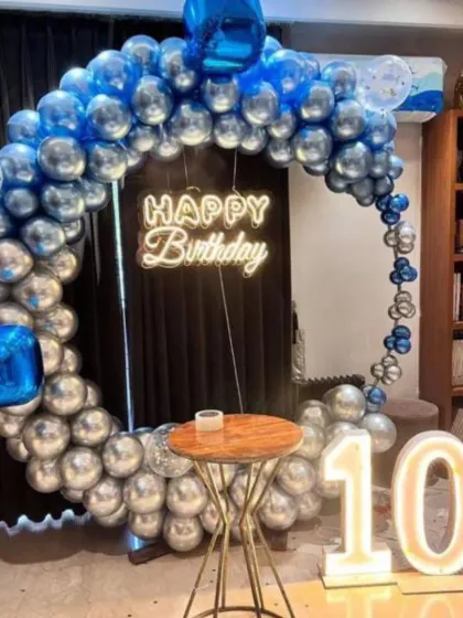 A cool blue and silver theme for a 10th birthday. This setup includes a circular balloon arch, a 'Happy Birthday' neon sign, and a light-up marquee number '10'.