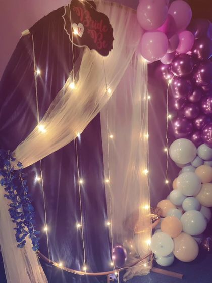A full view of the elegant backdrop I created for a bridal shower, featuring a draped arch, fairy lights, and a multi-colored balloon garland.