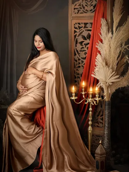 A quiet moment of reflection. This mom-to-be, draped in a golden satin saree, looks down at her bump with love, surrounded by the warm glow of candles.