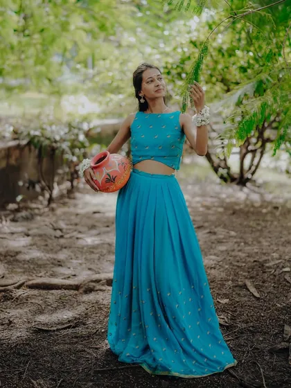 A full-length portrait in a lush green setting, where the model as Radha holds a matka, creating a classic, pastoral scene.