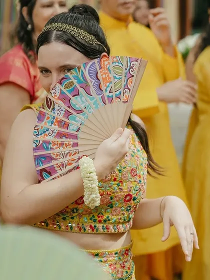 A guest playfully peeks from behind a colorful fan during the Haldi festivities.