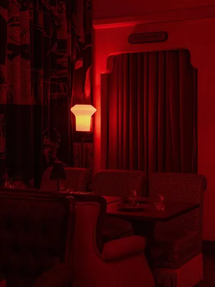An intimate dining nook, framed by a curtained archway. The red light creates a sense of privacy and drama.