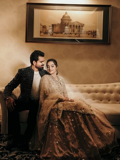 An elegant reception portrait. The couple is posed on a classic sofa, looking relaxed and happy, showcasing their beautiful evening attire in a sophisticated setting.