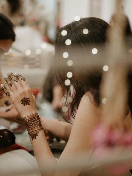 An artistic shot of the mehendi application, seen through a string of fairy lights, capturing the magic of the moment.