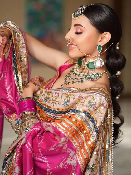 A candid and joyful shot of a Punjabi bride. The makeup is kept fresh and radiant, with a focus on a natural glow that complements her vibrant outfit and happy expression.
