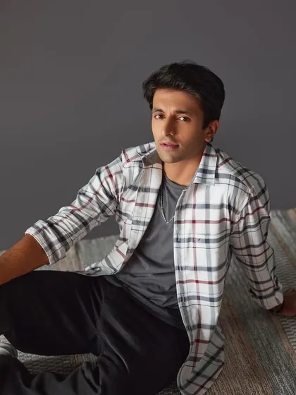 A catalogue shot for a men's casual wear brand. The makeup is minimal and clean, focusing on shine control and evening out the skin tone for a polished final image.