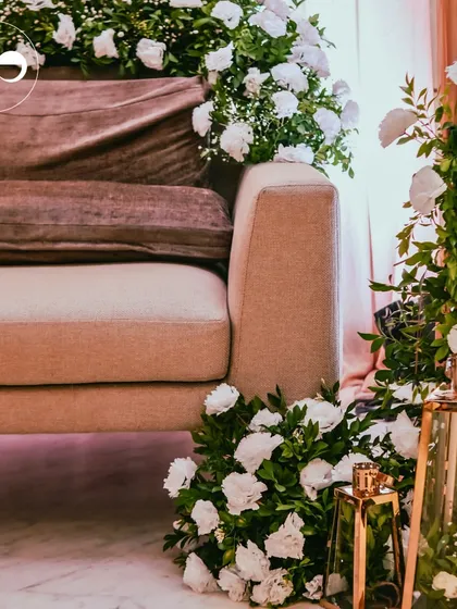 A close-up of the main seating area for a Roka, adorned with cascades of white roses and baby's breath. The gold lanterns add a touch of warm, ambient light to the elegant setup.