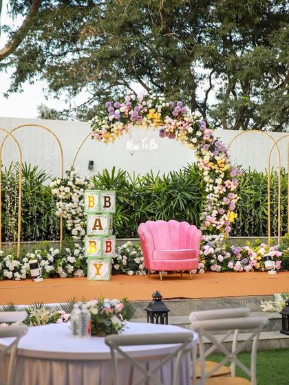 The stage is set for a baby shower with a beautiful floral arch and a pink "Mom To Be" chair. The decor is both sweet and sophisticated.