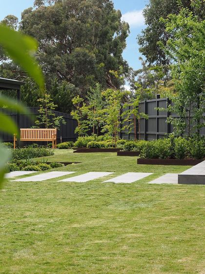 A minimalist backyard design with a large, open lawn and clean-edged garden beds. Concrete stepping stones create a simple, functional path across the grass.