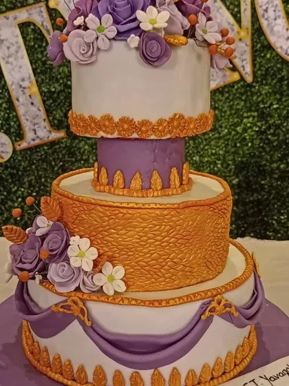 A grand, multi-tiered cake designed for a royal-themed celebration. The combination of purple and gold, intricate patterns, and floral arrangements creates a truly majestic and unforgettable centerpiece.