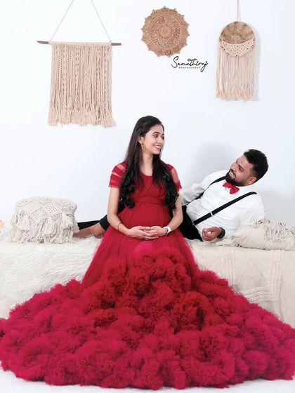 A romantic couple portrait in a boho-inspired studio setting. The red gown adds a vibrant touch to the otherwise neutral and earthy decor.