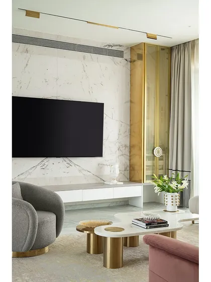 The TV unit in this living room is designed to be both functional and beautiful. The clean white console sits below a striking marble wall, flanked by a custom brass storage cabinet that adds a luxurious touch.
