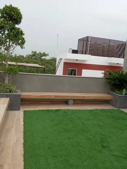 A minimalist rooftop garden in GK1 featuring a clean patch of artificial lawn next to a wooden deck. A long, low-profile wooden bench is integrated into the design, providing simple and functional seating.