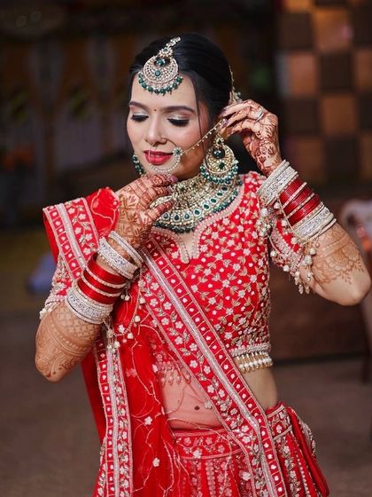 Adjusting the final details. This candid shot captures the bride as she perfects her jewellery, showing off the detailed eye makeup and intricate mehndi.