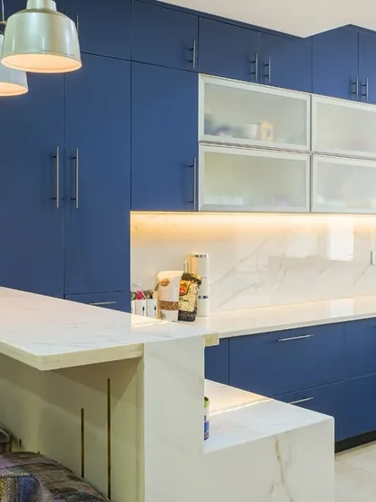 I design kitchens that are a joy to live and cook in. This modern kitchen uses a bold blue on its cabinetry, paired with sleek white marble and a functional breakfast bar to create a striking, elegant, and highly practical culinary space.