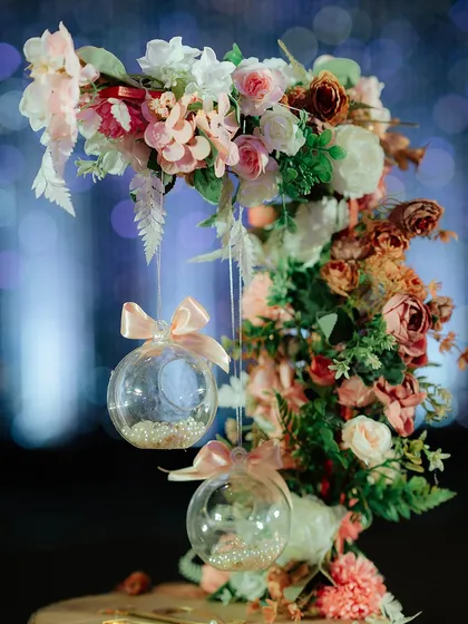 A close-up of a hanging floral detail. Clear baubles filled with pearls are suspended from a pastel floral arrangement, adding a delicate and whimsical touch to the decor.