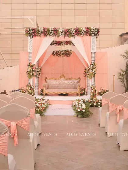A wide view of a beautiful rooftop wedding setup. The peach-themed mandap, elegant guest seating with matching sashes, and floral aisle create a cohesive and romantic atmosphere.