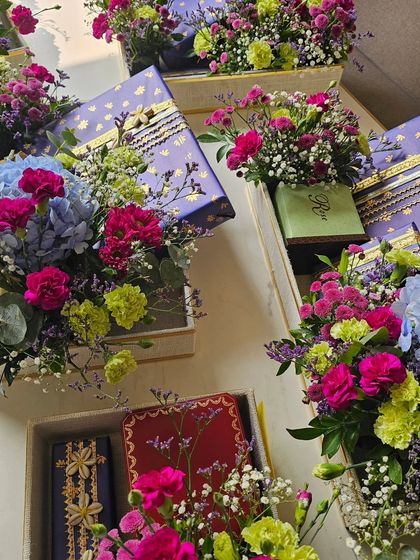 An overhead shot capturing the beautiful hustle of wedding season. Multiple gift hampers are ready to go, each one a unique composition of colorful flowers and elegantly wrapped presents.