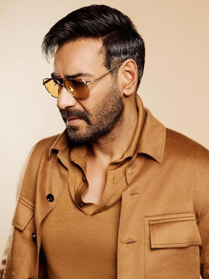 A close-up of Ajay Devgn in a monochromatic brown Zegna outfit for a movie premiere, with yellow-tinted glasses adding a vintage touch.