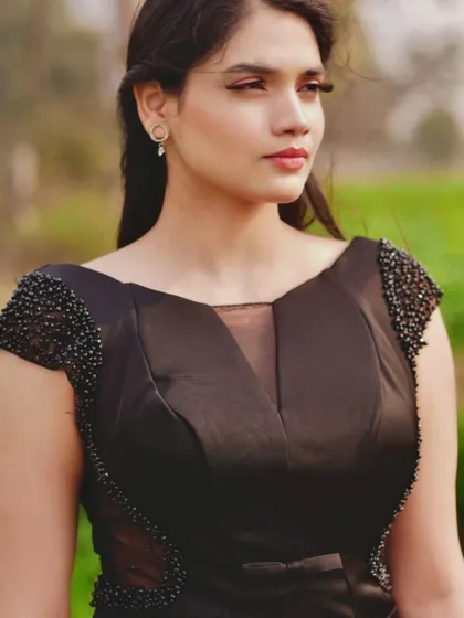 A close-up portrait showcasing the detailed craftsmanship of this custom black gown. The hand-beaded cap sleeves and sheer illusion neckline add a touch of sparkle and sophistication, framing the face beautifully.