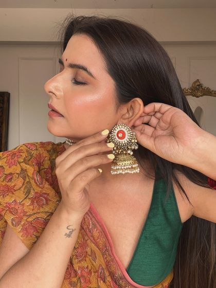 A close-up showing the harmony between the makeup and traditional accessories. The skin has a beautiful, healthy glow, and the eye makeup is subtle enough to let the statement jhumkas shine.