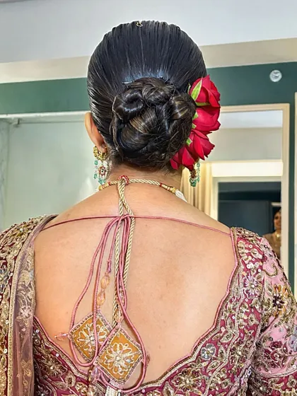 A close-up of the intricate red rose bun, a bold and beautiful choice that complements her pink lehenga perfectly.