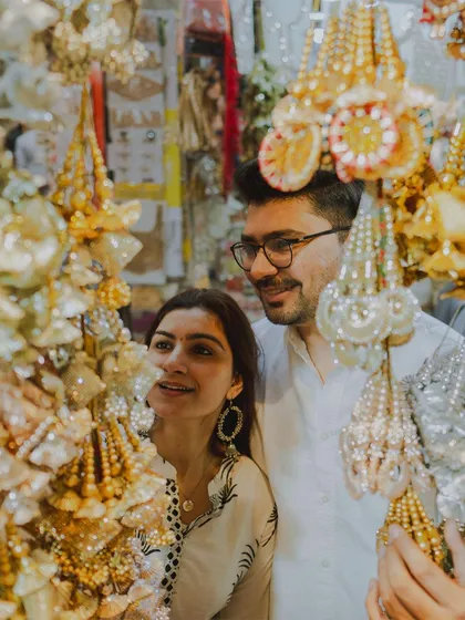 A couple admires traditional wedding accessories in a bustling market, a unique concept for a pre-wedding shoot.