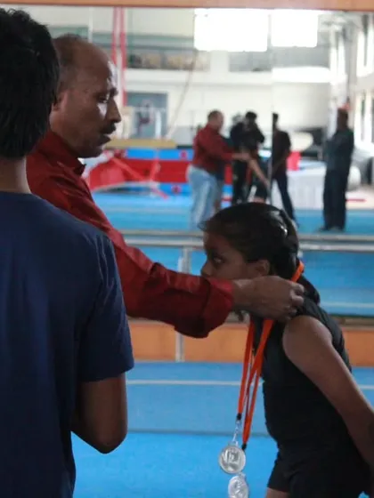A coach awarding a medal to a proud gymnast at the Dasara District Level Selection. A moment of recognition for her dedication.