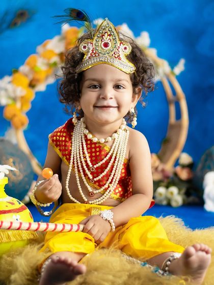 This smiling little Krishna is holding a sweet treat, adding an extra layer of cuteness to the photo.