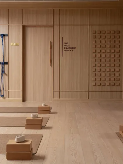 The yoga studio, a study in the geometry of stillness. The clean lines of the wood-paneled walls and the orderly arrangement of mats and blocks create a focused and peaceful environment.
