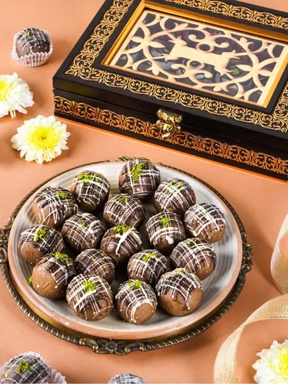 A plate of chocolate and nut ladoos next to a beautifully crafted wooden gift box. The warm, earthy tones and simple styling highlight the product's quality.