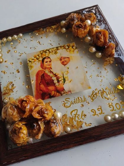 This is a square wooden frame filled with resin to preserve a couple's wedding flowers. I added their photo, names, and wedding date, with pearl details for an elegant touch.