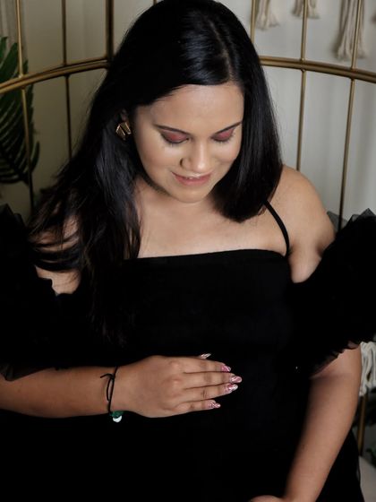 A quiet, contemplative moment. This close-up shot focuses on the mom-to-be looking down at her bump, dressed in a chic black off-the-shoulder gown.